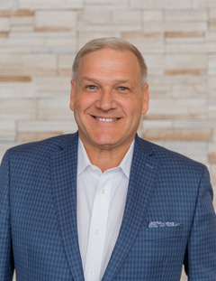 Lane Jones smiles at the camera in front of a light brick wall.