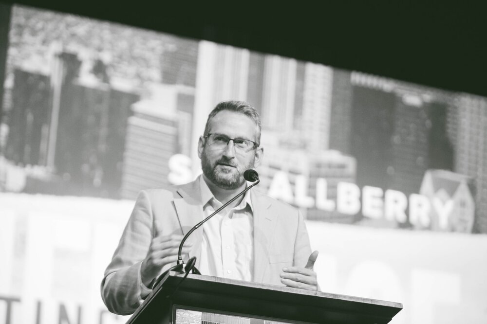 Sam Allberry stands on a stage speaking behind a pulpit.